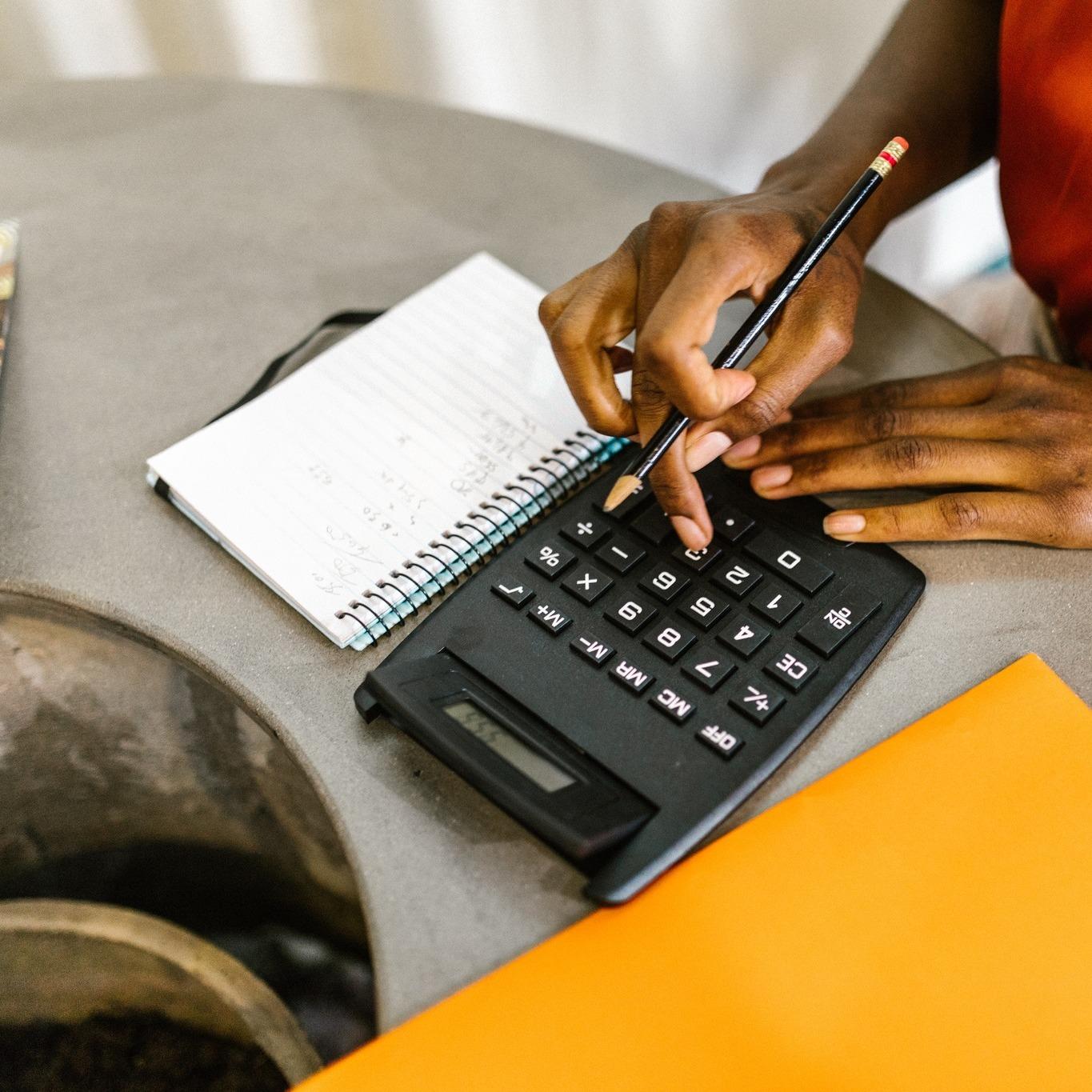 A lady is doing sums on a calculator and taking notes in a notepad