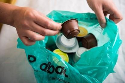 Someone is putting coffee capsules into a green podback bag