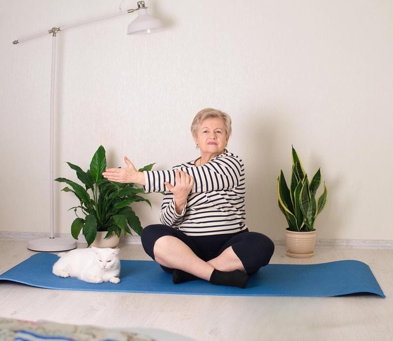 A mature lady is doing seated yoga next to her cat