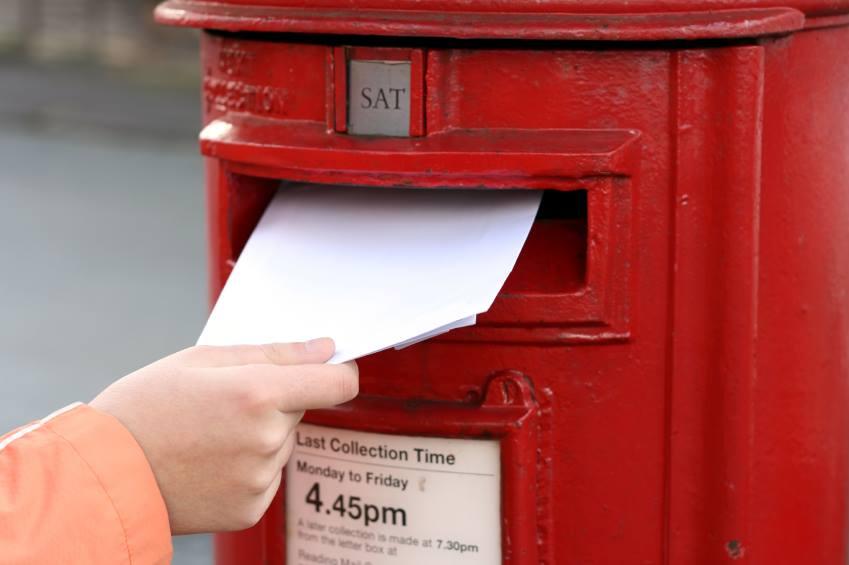 Someone's hand putting a letter in a red letterbox
